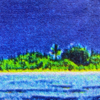 CALMECS T-SHIRT IN COLOR WHITE WITH TROPICAL ISLAND BACK PRINT. CLOSE-UP ISLAND VIEW WITH BLUE SKY.