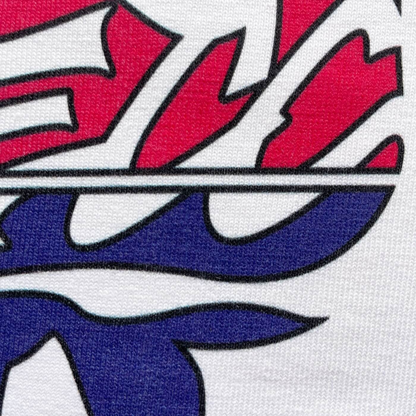 CALMECS T-SHIRT IN COLOR WHITE WITH RED AND BLUE DROMEDARY / CAMEL AND CALMECS LOGO FRONT PRINT. CLOSE UP CALMECS FONT.