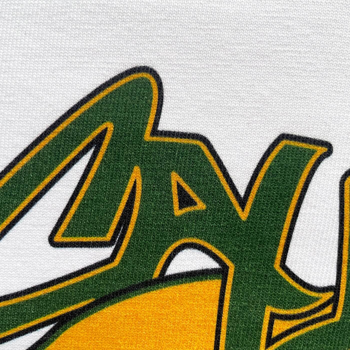 CALMECS T-SHIRT IN COLOR WHITE WITH YELLOW / ORANGE KANGAROO AND GREEN CALMECS LOGO FRONT PRINT. CLOSE UP CALMECS LOGO.