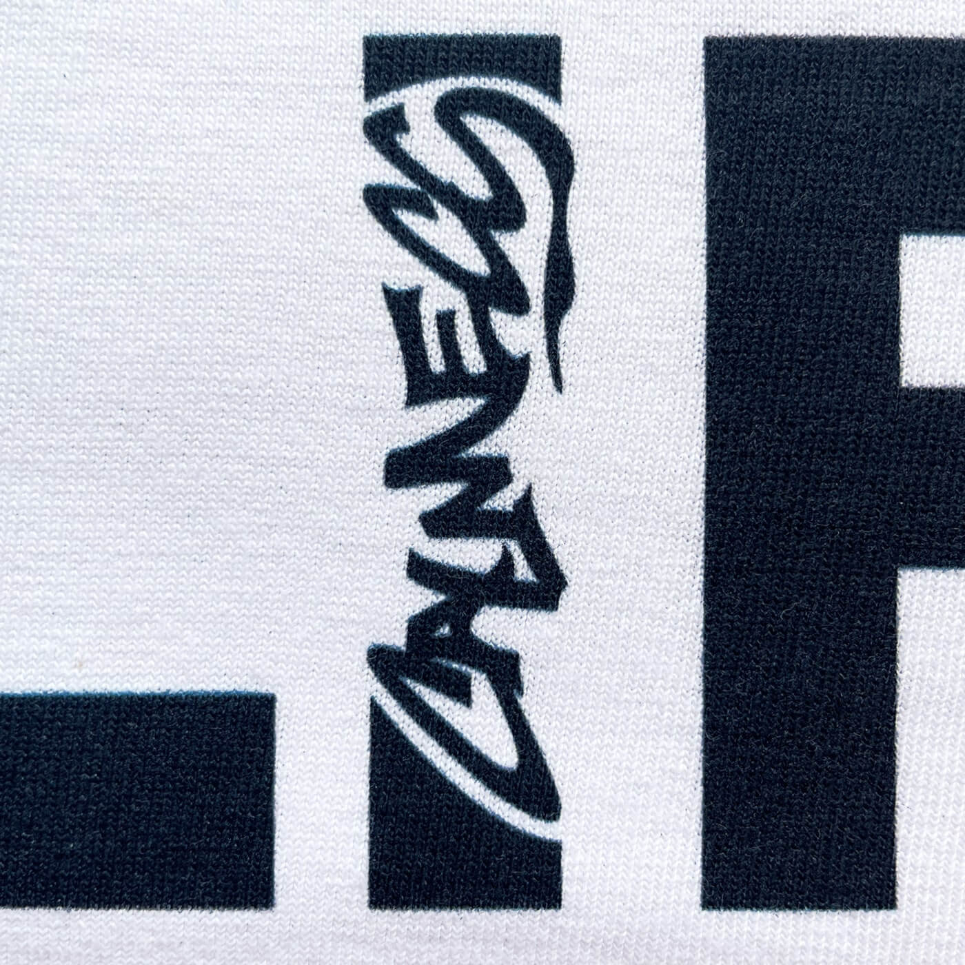 CALMECS T-SHIRT IN COLOR WHITE WITH BLACK LIFE-LIFE BALANCE FONT FRONT PRINT. CLOSE UP CALMECS LOGO.