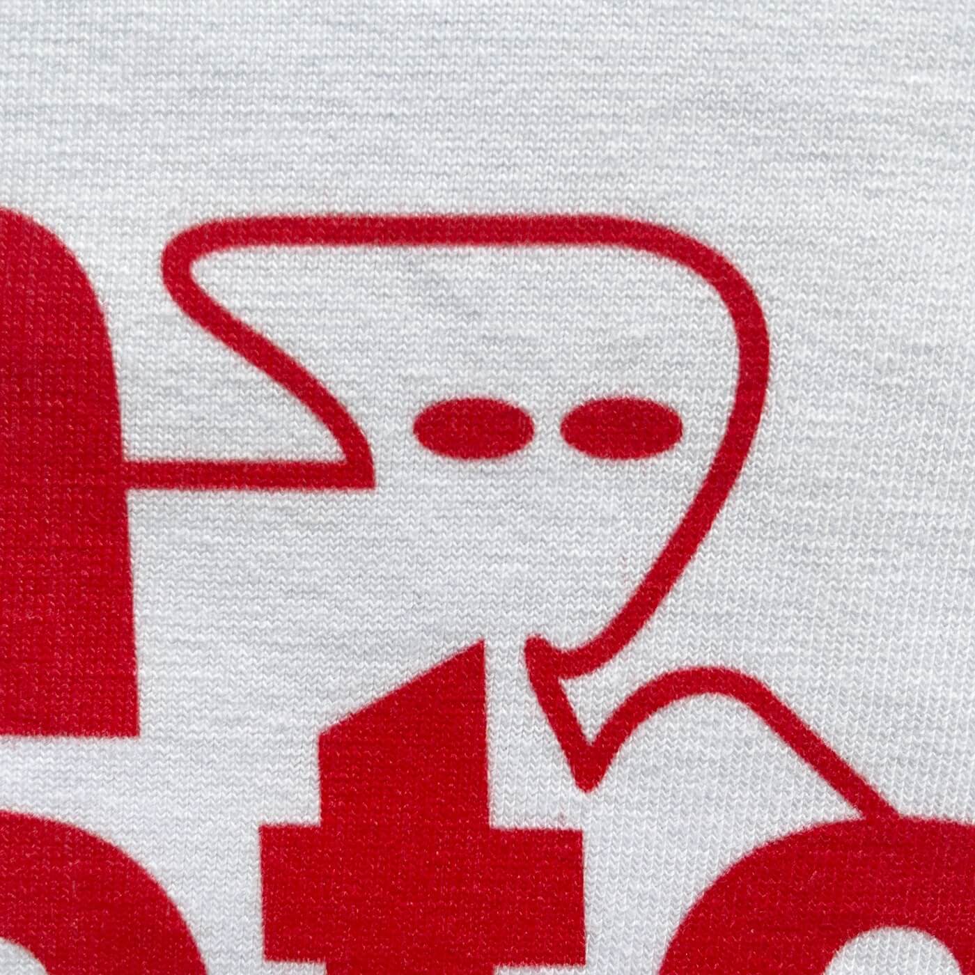 CALMECS T-SHIRT IN COLOR WHITE WITH RED MAIN CHARACTER FONT FRONT PRINT. CLOSE UP CALMECS LOGO.