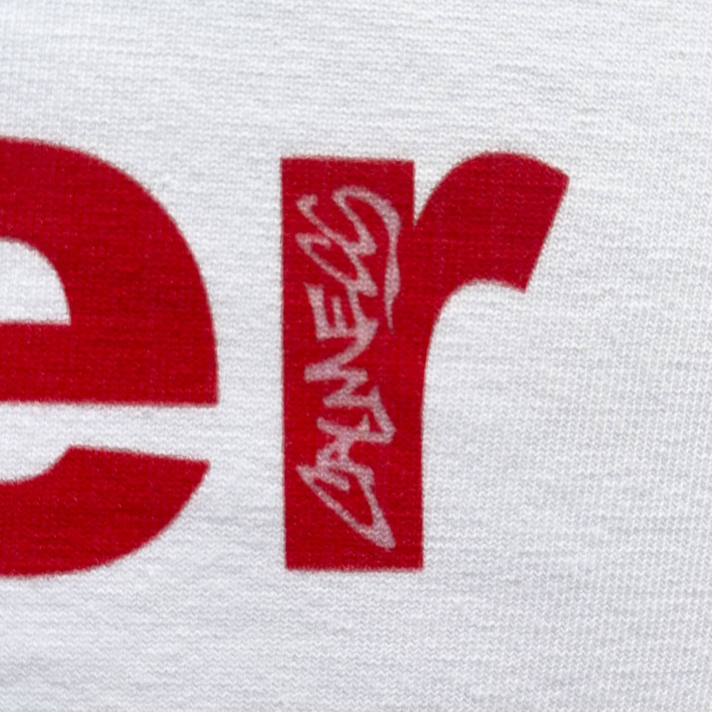 CALMECS T-SHIRT IN COLOR WHITE WITH RED MAIN CHARACTER FONT FRONT PRINT. CLOSE UP CALMECS FONT.