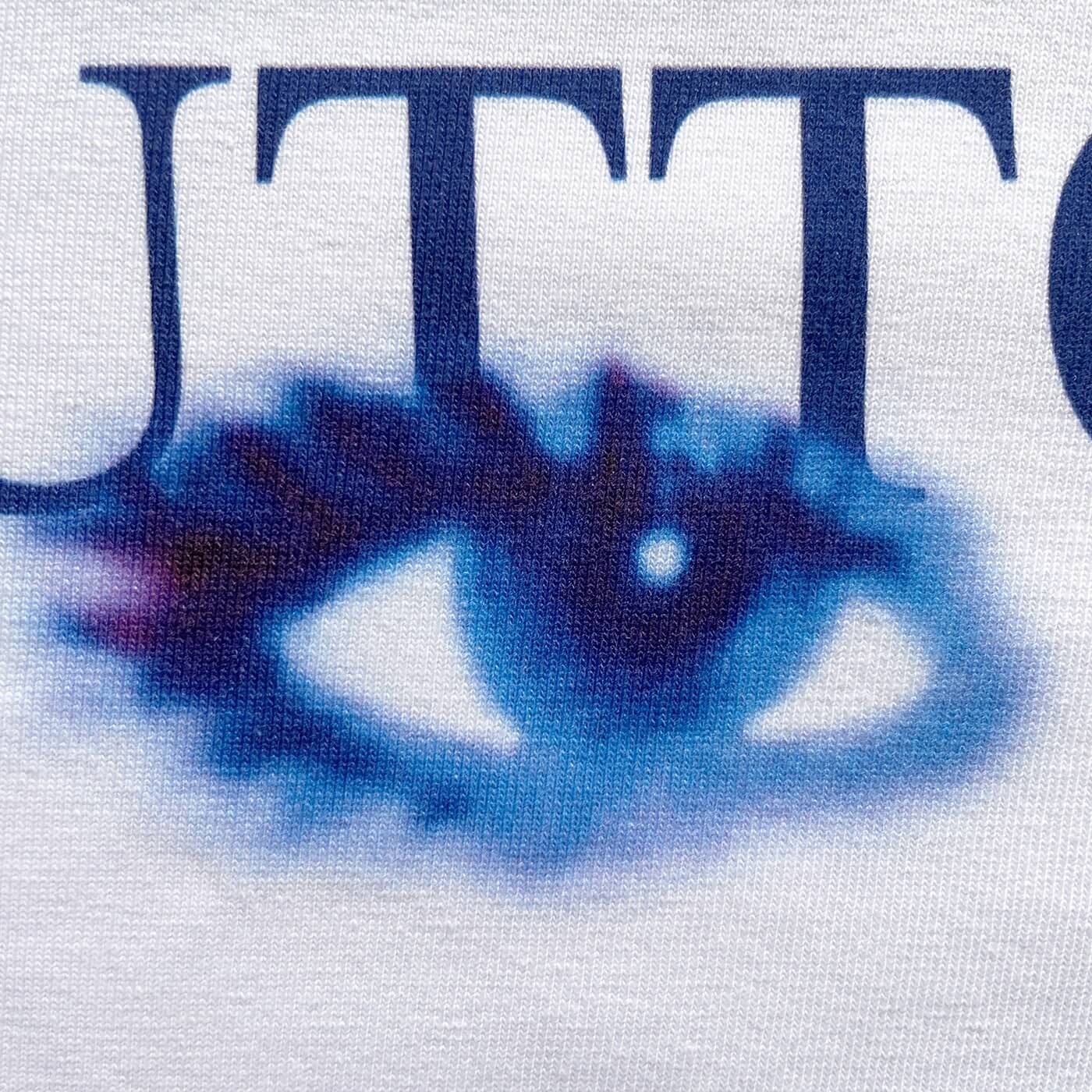 CALMECS T-SHIRT IN COLOR WHITE WITH BLUE TUTTO PASSA FONT AND BLUE EYES FRONT PRINT. CLOSE UP LEFT EYE.